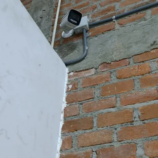 Cámara de seguridad tipo bullet instalada en pared exterior de ladrillo, J&T Express